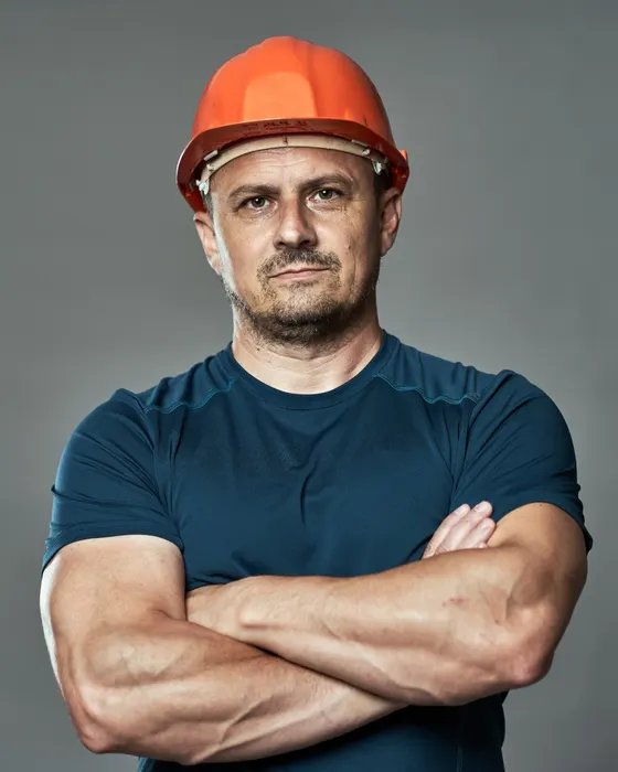 A construction worker in an orange hard hat stands with his arms crossed